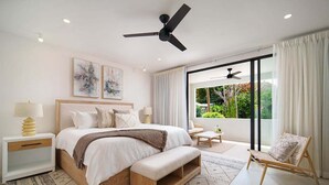A modern bedroom with a large bed, bedside tables, a bench, a chair, and a view of greenery through large windows. - NEW villa with plunge pool, 3 mins to beach - Sorrento 10 (2 bed) (Lower Carlton)