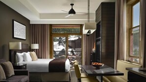 Ein Hotelzimmer mit Bett, Schreibtisch, Stuhl, Sofa, einem Esstisch mit Obstschale, Deckenventilator und Fenster mit Blick auf eine verschneite Landschaft.