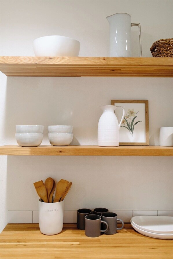 Uma estante na cozinha com tigelas brancas, um jarro branco e um quadro emoldurado.
