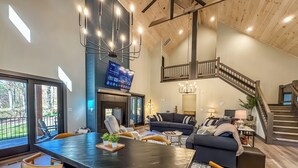A spacious living area with a large dining table, comfortable seating, a fireplace, and a staircase leading to an upper level. - Luxury + Close to slopes + Golf Side (McHenry)