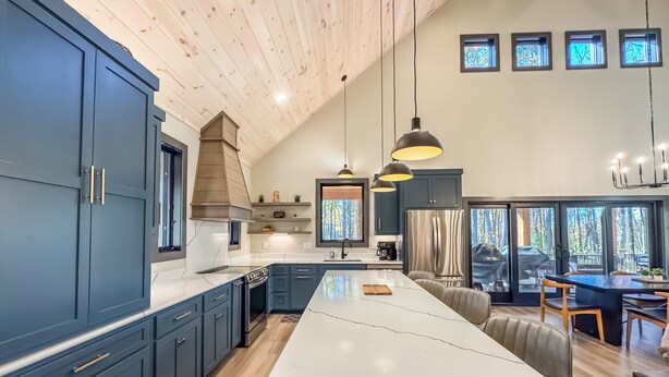 A modern kitchen with dark blue cabinets, a large island, and pendant lighting. - Luxury + Close to slopes + Golf Side (McHenry)