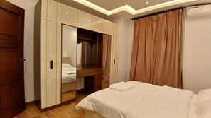 A bedroom with a bed, a wardrobe, a mirror, and a ceiling light fixture. - Alsawah 3BR Duplex with garden in Eastown sodic (New Cairo)