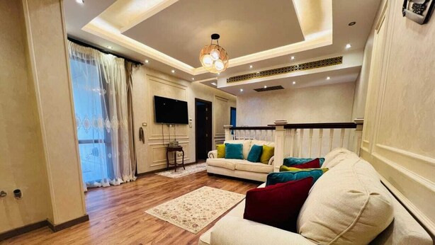 A modern living room with a sofa, a TV, and a chandelier. - Alsawah 3BR Duplex with garden in Eastown sodic (New Cairo)
