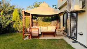 A covered outdoor seating area with a wooden bench, a table, and two chairs. - Alsawah 3BR Duplex with garden in Eastown sodic (New Cairo)