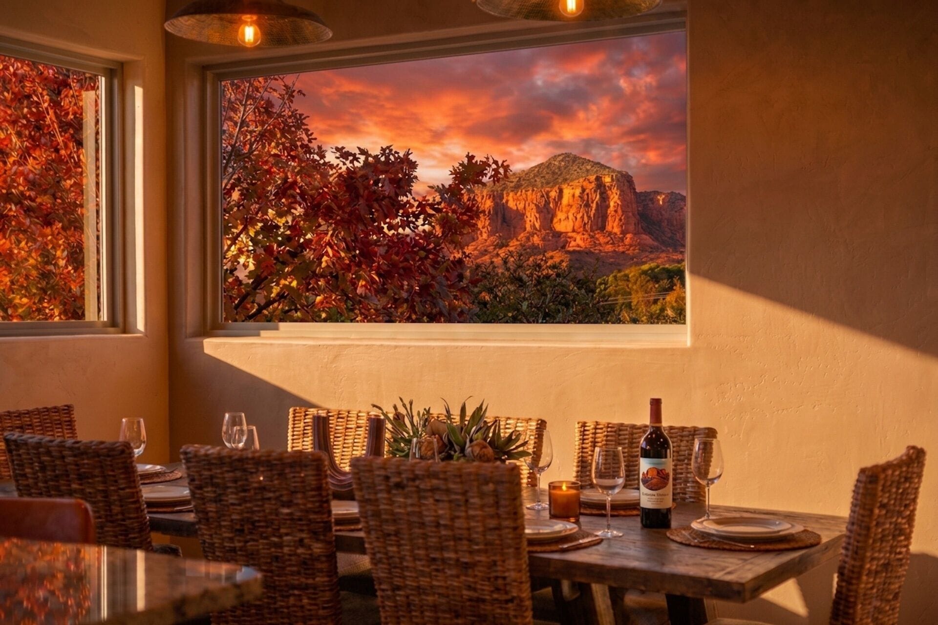 A dining area with wicker chairs, a table set for two, and a bottle of wine.