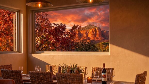 Un comedor con sillas de mimbre, una mesa dispuesta para dos personas y una botella de vino.