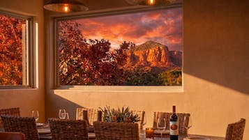 A dining area with wicker chairs, a table set for two, and a bottle of wine.