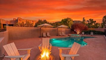 A pool area with lounge chairs, a fire pit, and umbrellas.