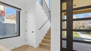 Ein modernes Interieur mit einer Holztreppe, einem großen Fenster und einer schwarzen Tür, die nach draußen führt.