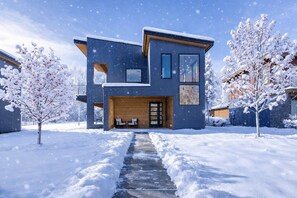 A modern two-story house with a stone pathway leading to the entrance, surrounded by snow-covered trees. - The Ridgehouse | Modern Mountain Stay with Sauna Near Trails & Skiing (Hailey)