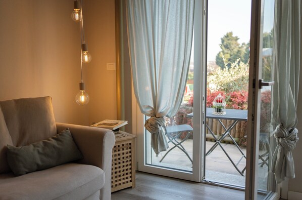 A room with a sofa, a small table, a basket, and a view through a glass door to an outdoor area with a table and chairs. - WellHome Asti (Asti)