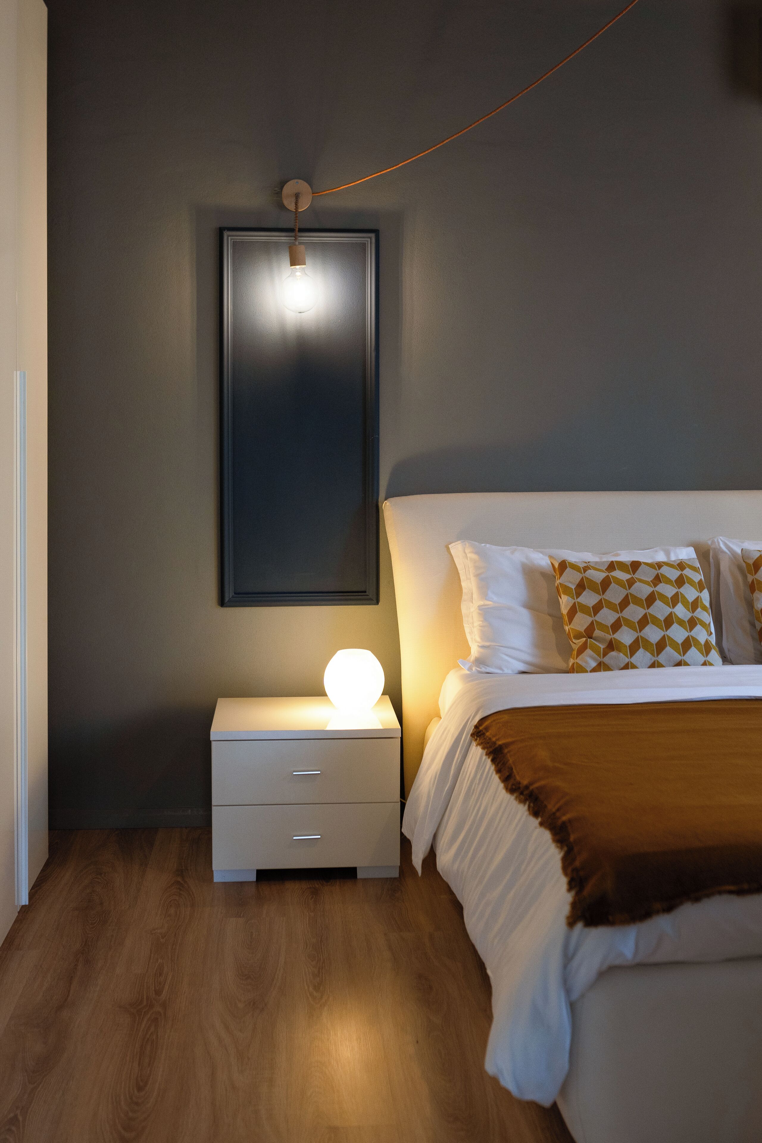 A bedroom with a bed, bedside table, and a wall-mounted light fixture.