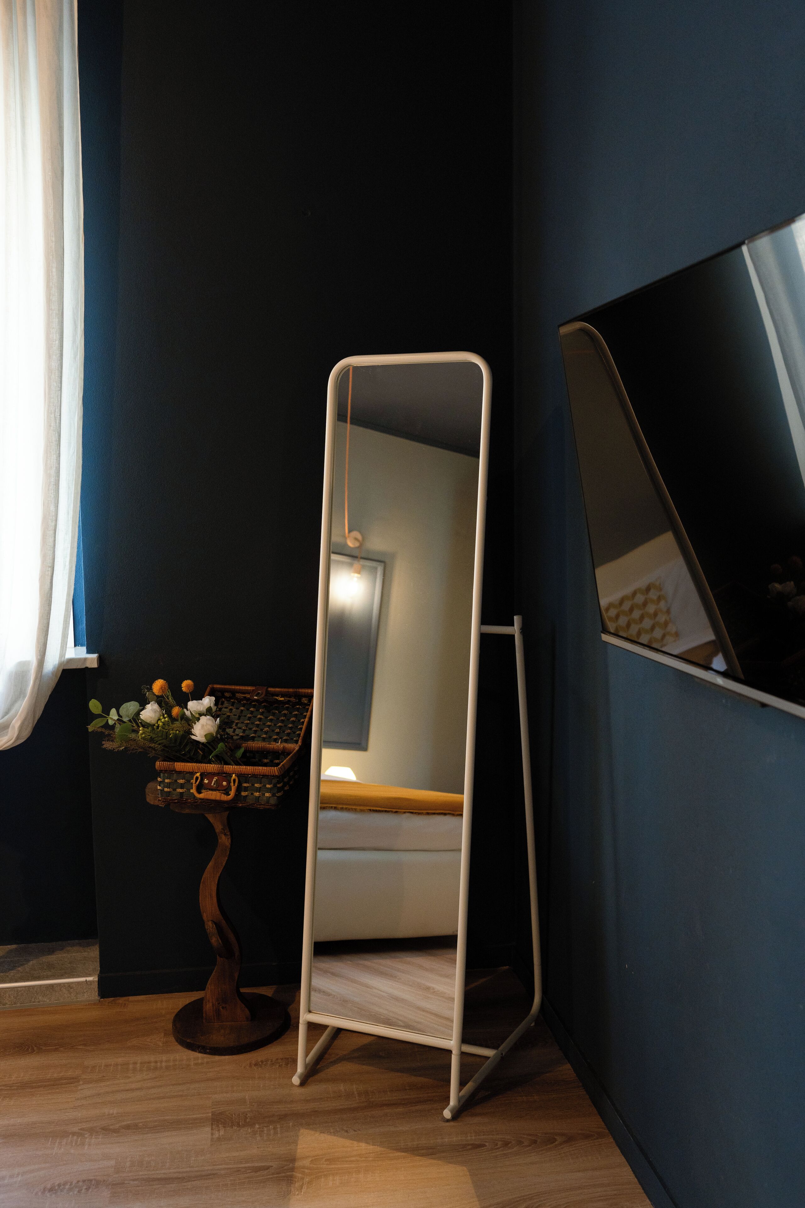 A room with a dark blue wall, a white chair, a small table with a basket of flowers, and a mirror leaning against the wall.
