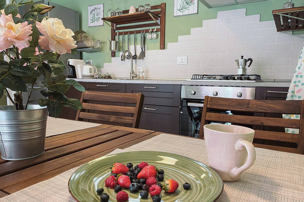 A kitchen with a dining table, chairs, a plate of berries, a potted plant, and kitchen appliances.