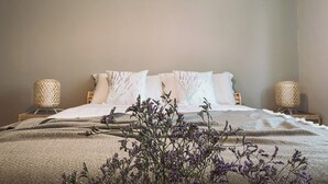 A neatly made bed with white linens and a lavender floral arrangement in front.