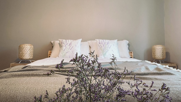 A neatly made bed with white linens and a lavender floral arrangement in front. - WellHome Asti (Asti)