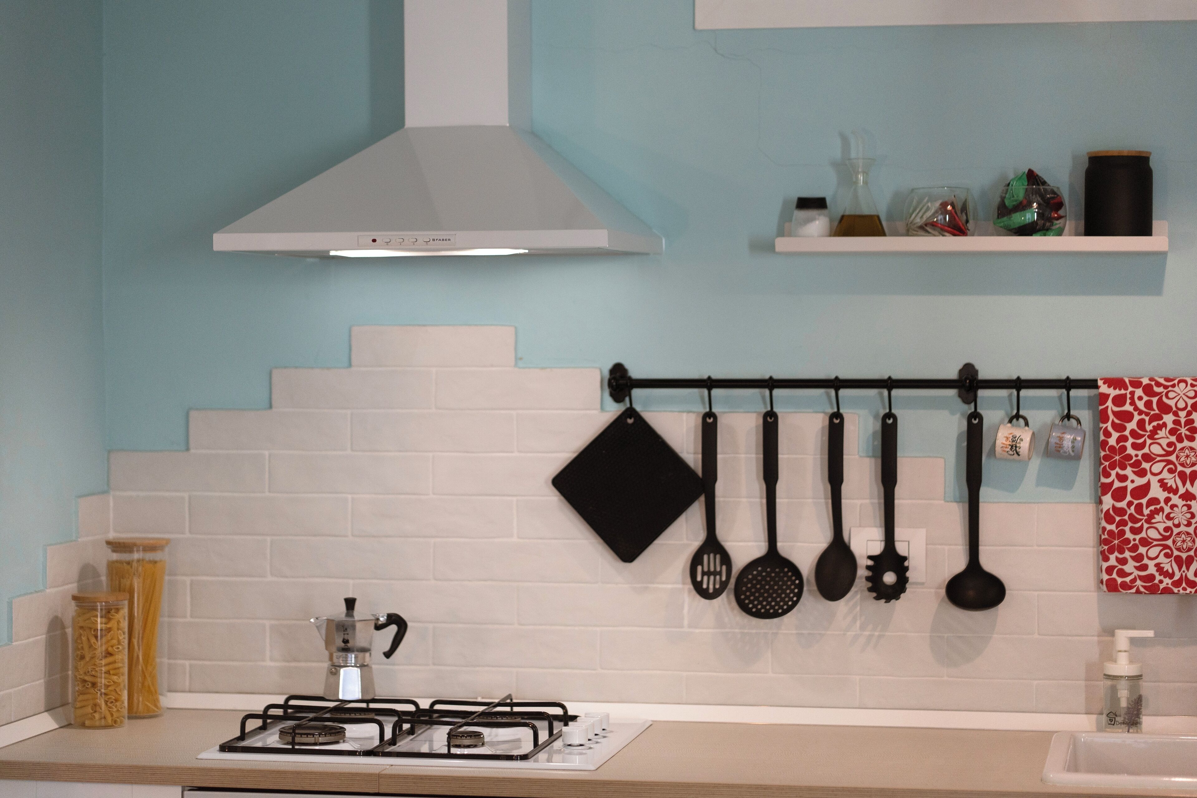 A kitchen with a gas stove, a white range hood, and various kitchen utensils hanging on a rack.