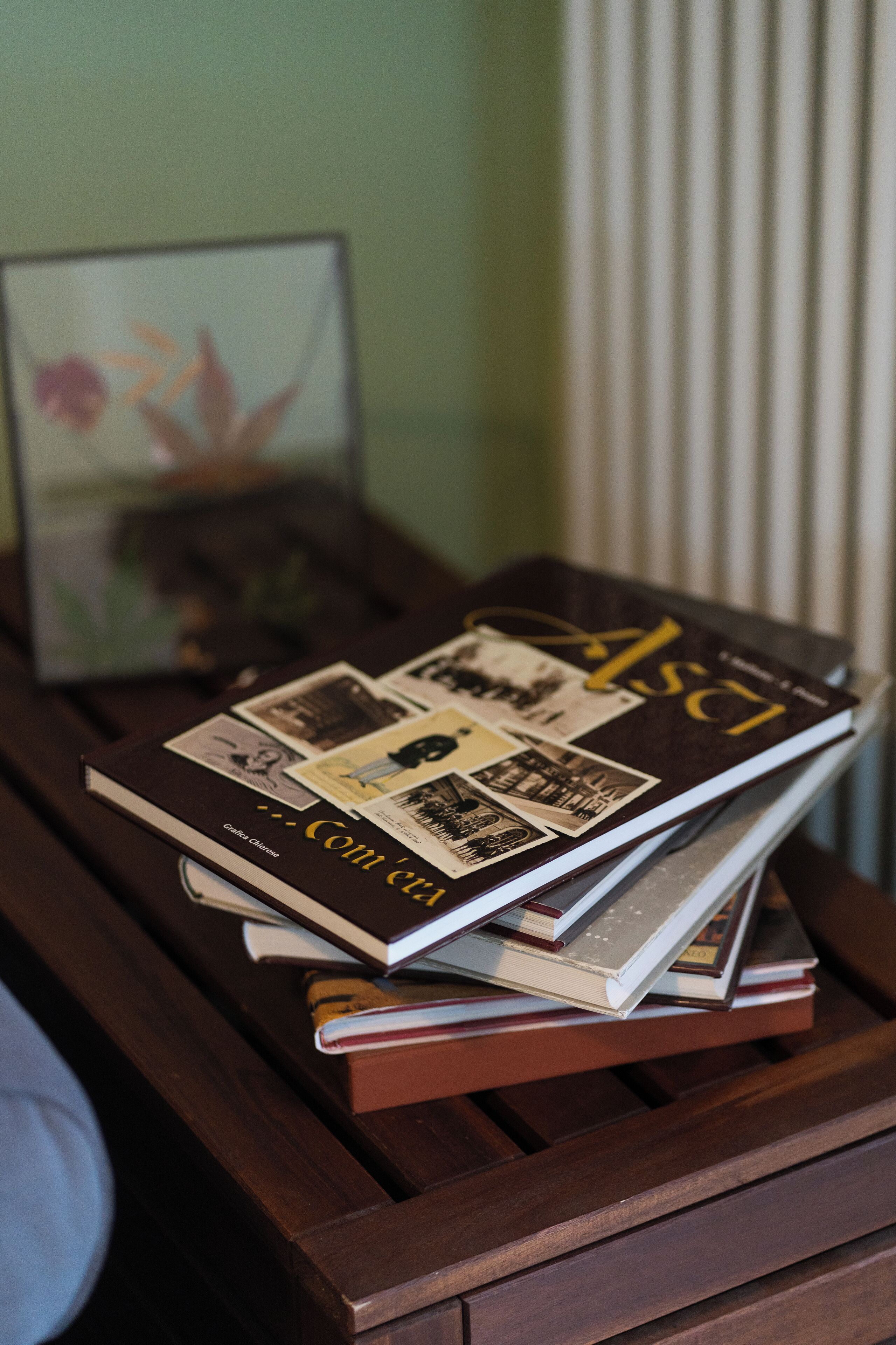 A stack of books on a wooden side table with a picture frame in the background.