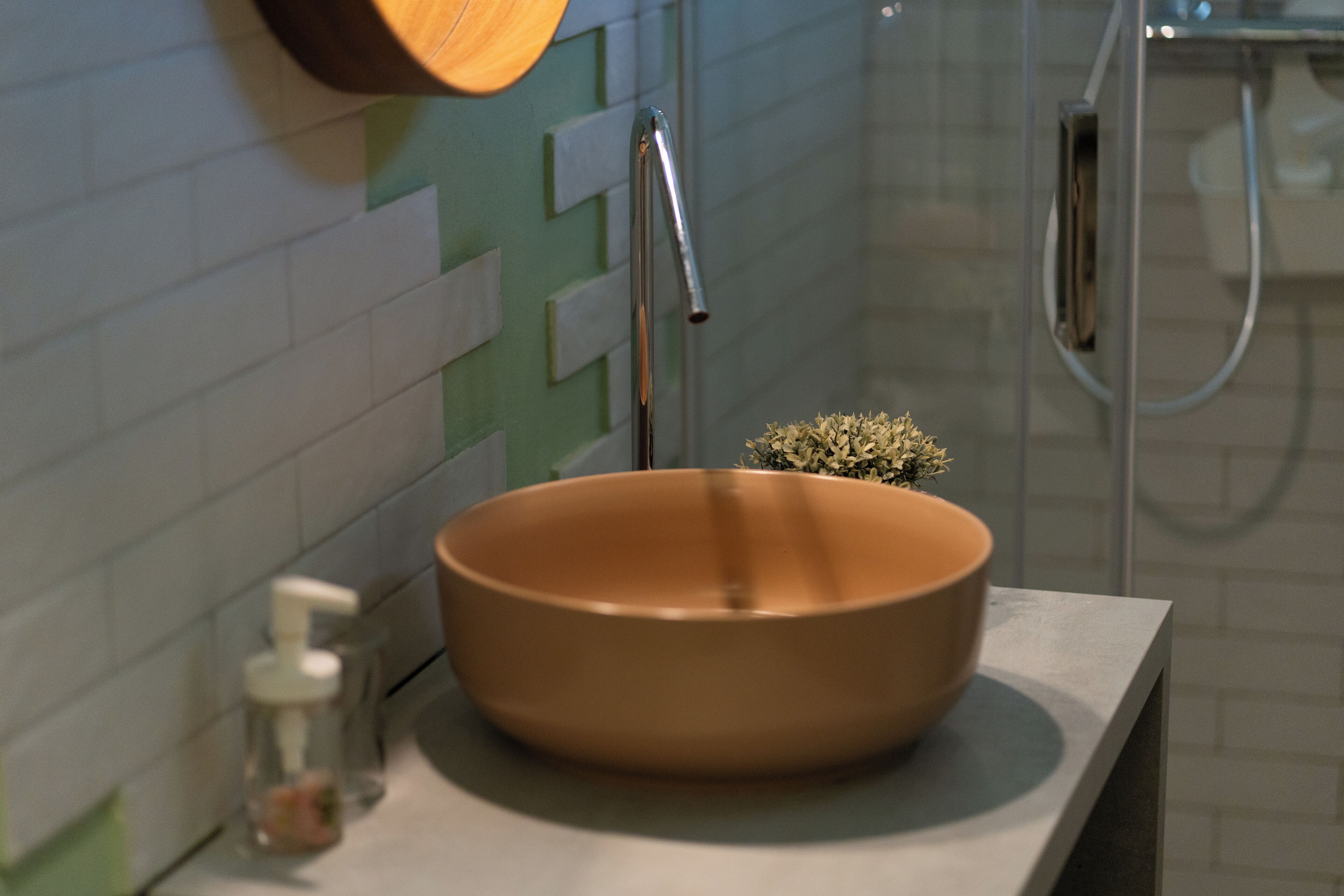 Une salle de bain avec un lavabo rond de couleur marron, un distributeur de savon en verre et un espace douche.
