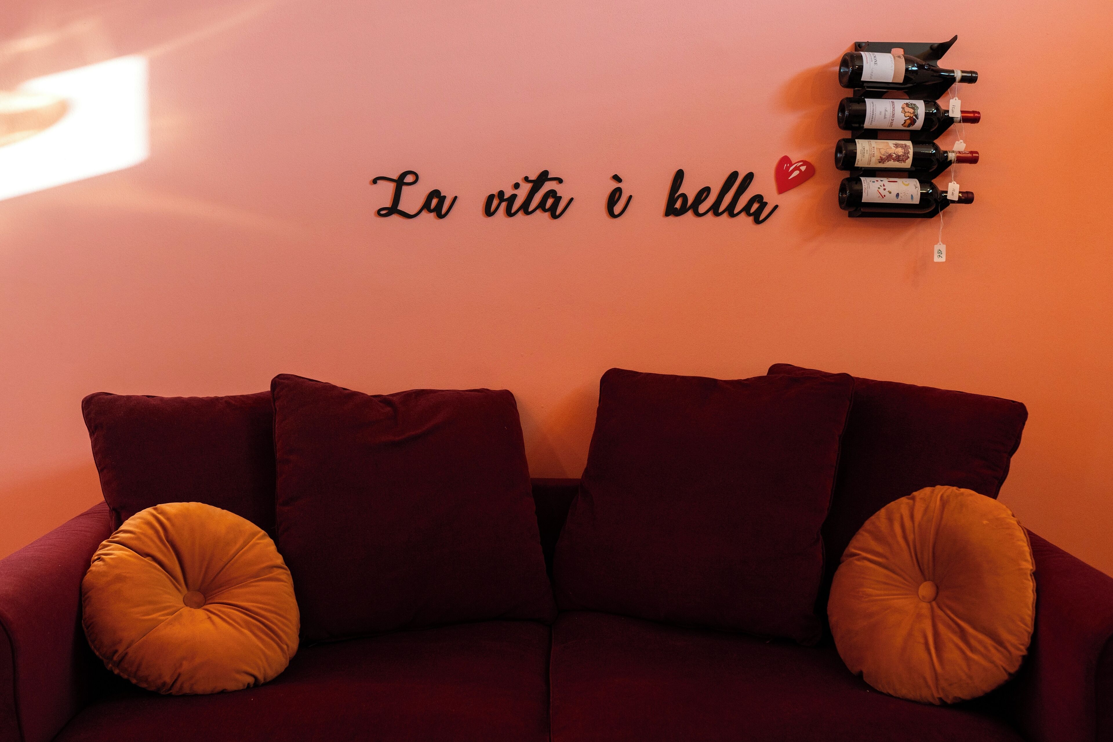 A red sofa with two yellow cushions and a wall with a wine rack and a sign that says "La vita è bella."