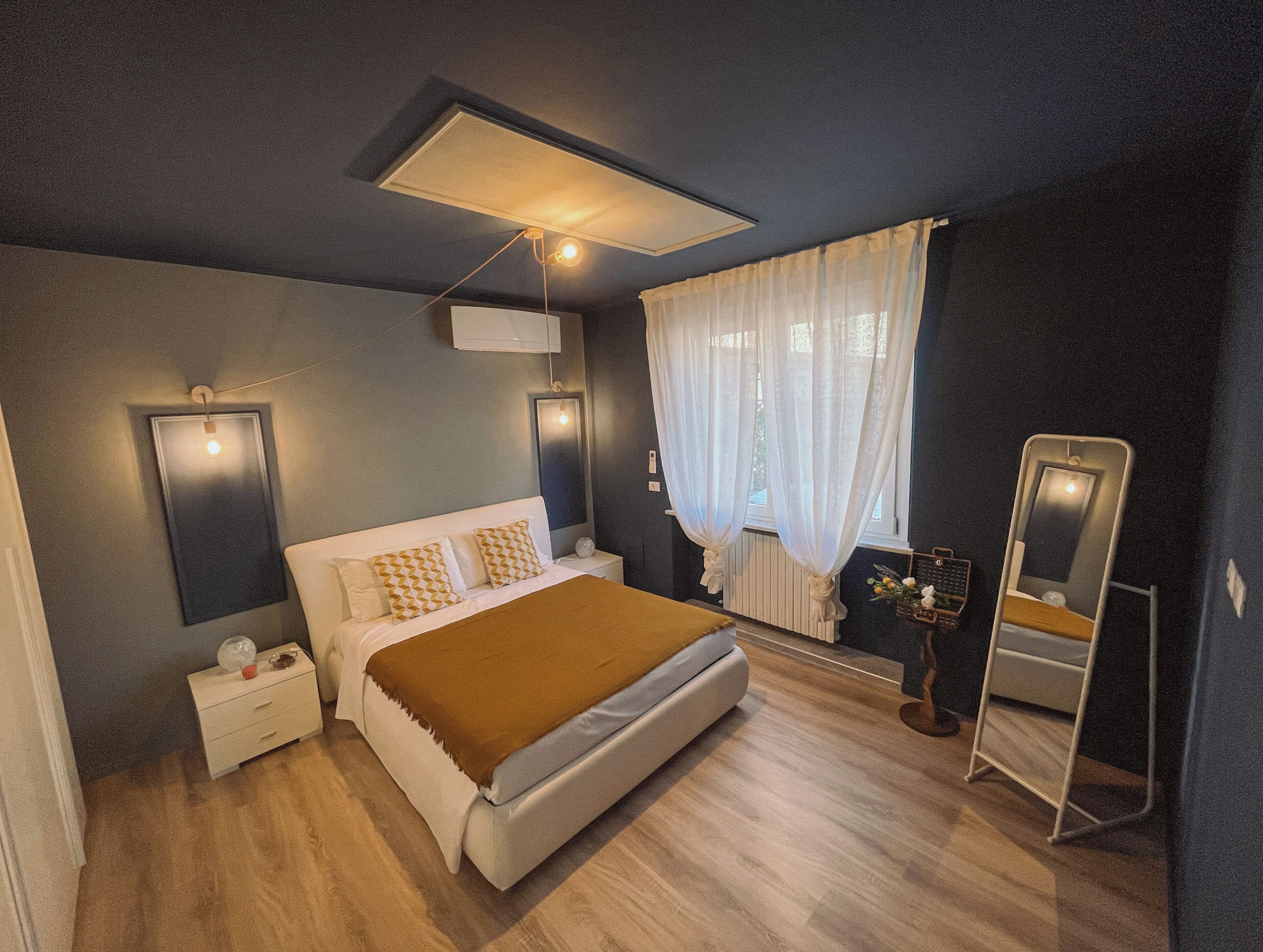 Une chambre à coucher moderne, comprenant un lit, des tables de chevet, un miroir et un luminaire au plafond.