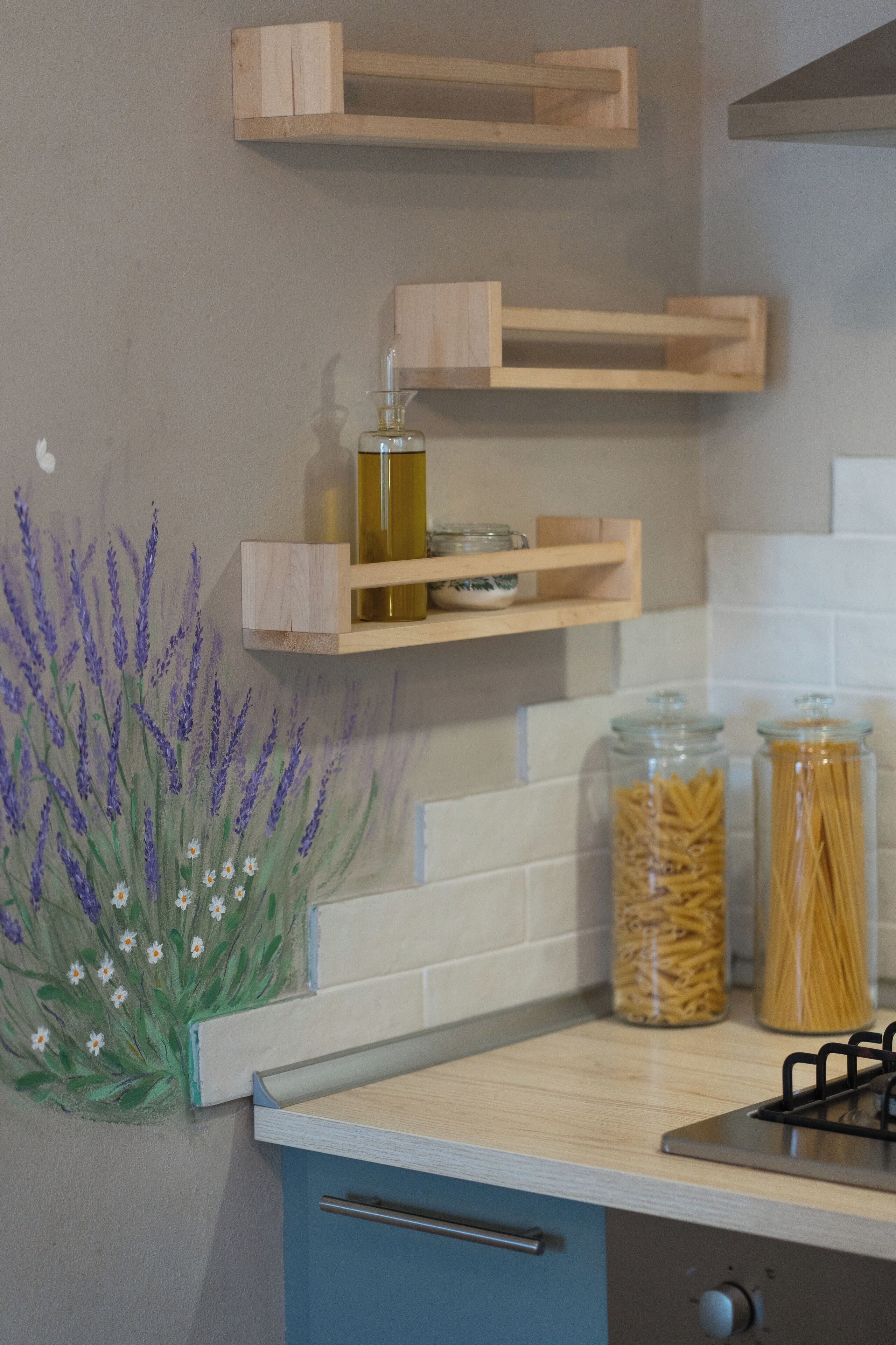 A kitchen with wooden shelves, a gas stove, and jars of pasta.
