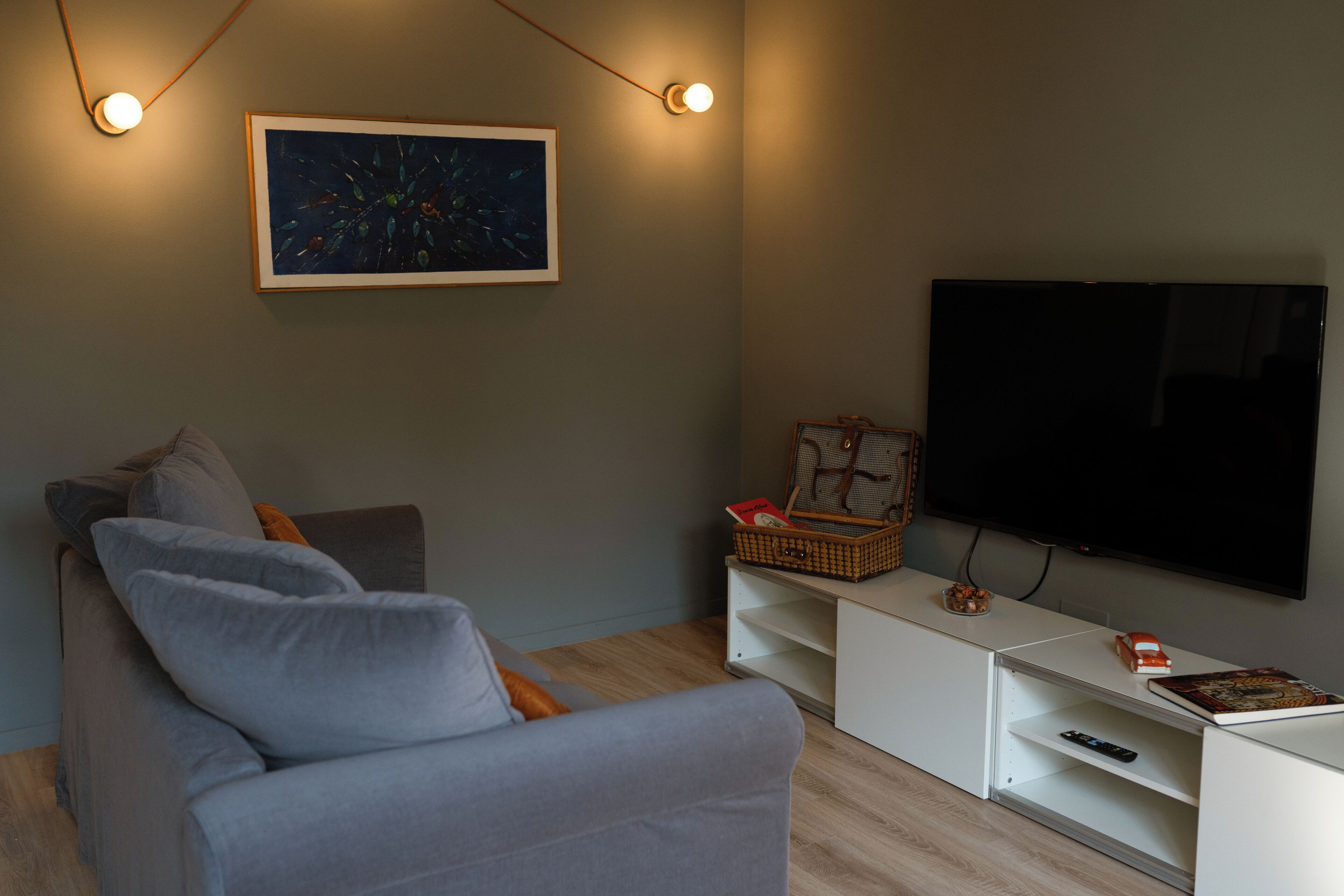 Ein modernes Wohnzimmer mit einem grauen Sofa, einem Flachbildfernseher und einem gerahmten Kunstwerk an der Wand.