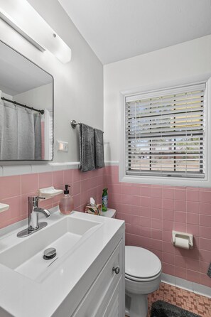 A bathroom with a white sink, a mirror, a toilet, and a window with blinds. - 3/1.5 Southern Grace (Dothan)