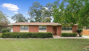 A two-story brick house with a front door, windows, and a small front yard with a hedge and a wooden fence. - 3/1.5 Southern Grace (Dothan)