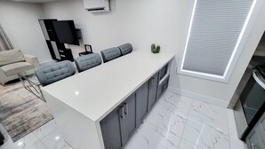Uma cozinha moderna com piso de mármore, uma ilha central com assentos, uma televisão de tela plana e um forno embutido.