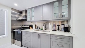Uma cozinha moderna com armários cinza, eletrodomésticos de aço inoxidável e bancada branca.