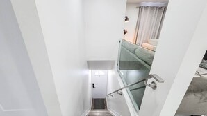 Uma escadaria com corrimão, uma porta no topo e vista de um quarto com cama e cortinas.