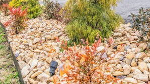 Ein Gebäude mit einer überdachten Veranda, Steinwänden und einem Garten mit verschiedenen Pflanzen und Steinen.