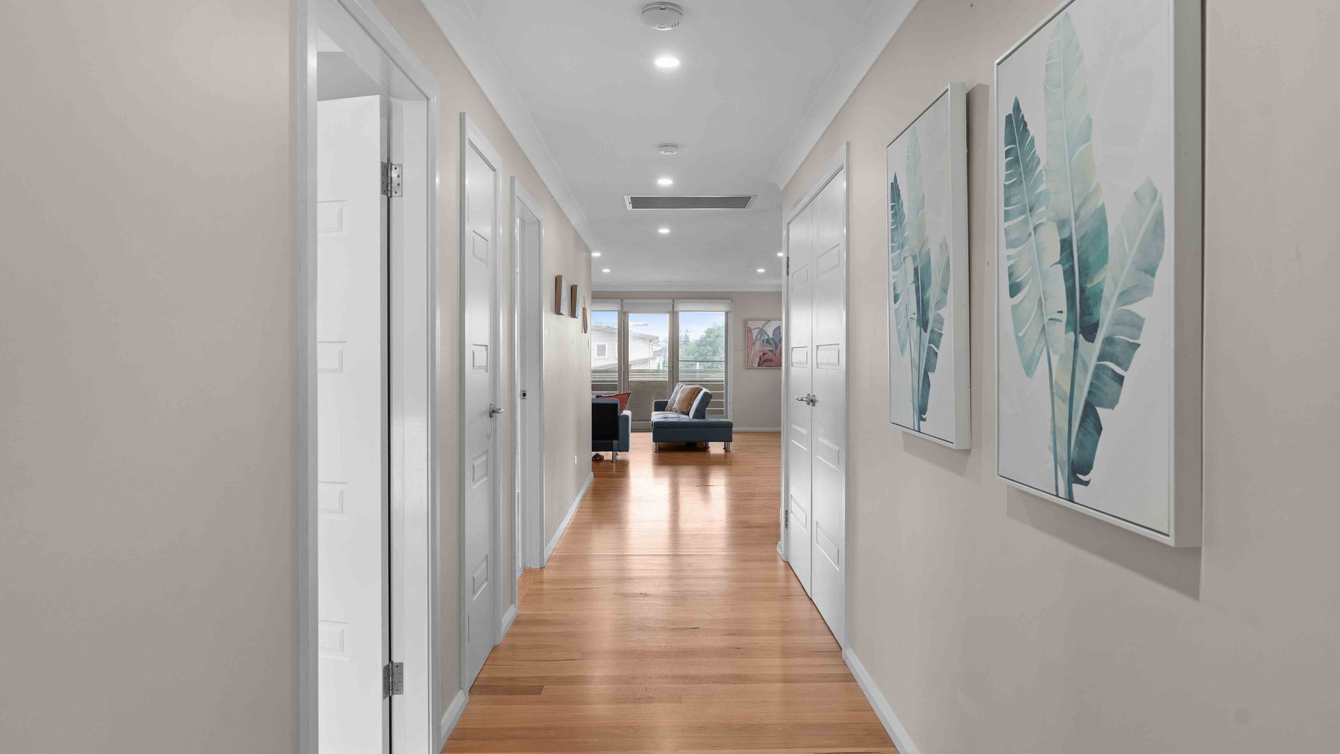 A hallway with wooden flooring, white doors, and artwork on the walls.