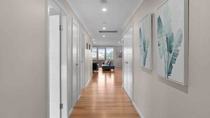 A hallway with wooden flooring, white doors, and artwork on the walls. - Beach Break Hideaway (The Entrance North)