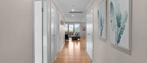 A hallway with wooden flooring, white doors, and artwork on the walls.