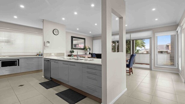 A modern kitchen with grey cabinets, a sink, and a clock on the wall. - Beach Break Hideaway (The Entrance North)