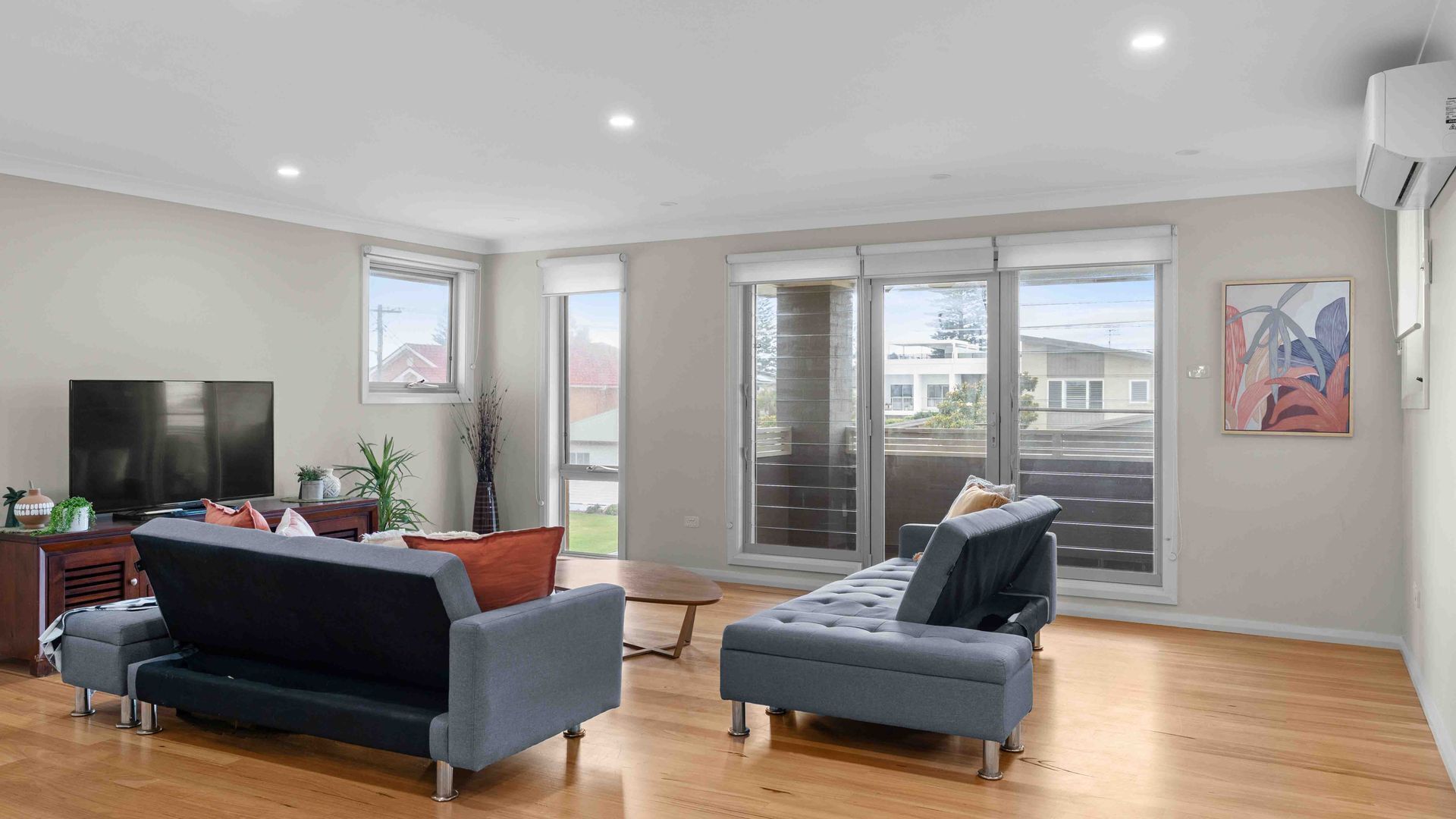 A modern living room with a flat-screen TV, two sofas, a coffee table, and a sliding glass door leading to a balcony.