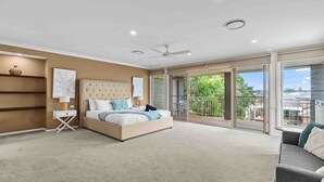 A spacious bedroom with a large bed, a ceiling fan, and a balcony with a view of the neighborhood. - Beach Break Hideaway (The Entrance North)
