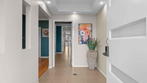 A hallway with a modern design, featuring a large vase, a painting, and a door with a security camera. - Beach Break Hideaway (The Entrance North)