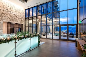 Un hall d’entrée moderne avec un mur en pierre, des portes en verre et une vue sur l’espace extérieur aménagé pour s’asseoir.
