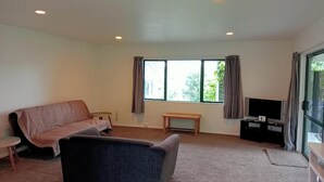 Ein Wohnzimmer mit einer Couch, einem Fernseher, einem kleinen Tisch und einem Fenster mit Vorhängen.
