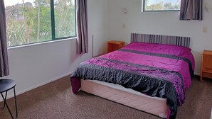 Ein Schlafzimmer mit Bett, Fenster, Heizkörper und einem kleinen Tisch.