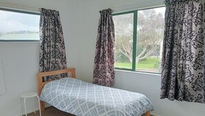 Ein Schlafzimmer mit einem Einzelbett, einem kleinen weißen Hocker und einem fenster mit Vorhängen.