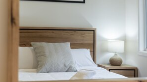 A neatly made bed with a wooden headboard, a bedside lamp, and a window to the right. - Lemon & Myrtle Cottage (Myrtleford)
