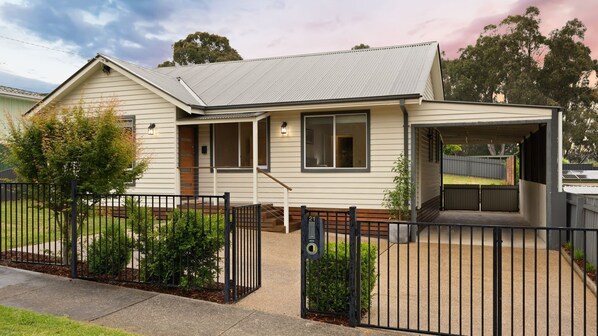 A single-story house with a covered porch, a fenced yard, and a small front yard. - Lemon & Myrtle Cottage (Myrtleford)