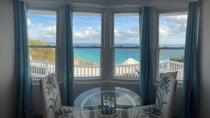 A corner room with a bay window overlooking a beach and ocean.