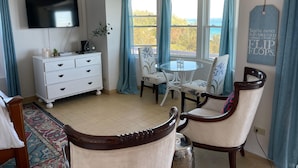 A room with a TV, a white dresser, a round table with chairs, a view of the sea, and a 'You're never fully dressed without a pair of flip flops' sign.