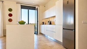 Une cuisine moderne dotée d’un îlot central, d’appareils électroménagers en acier inoxydable et offrant une vue à travers une porte vitrée.