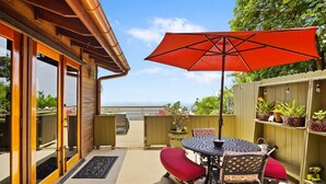 Una terraza de madera con una mesa, sillas y un paraguas rojo, con vista al océano.
